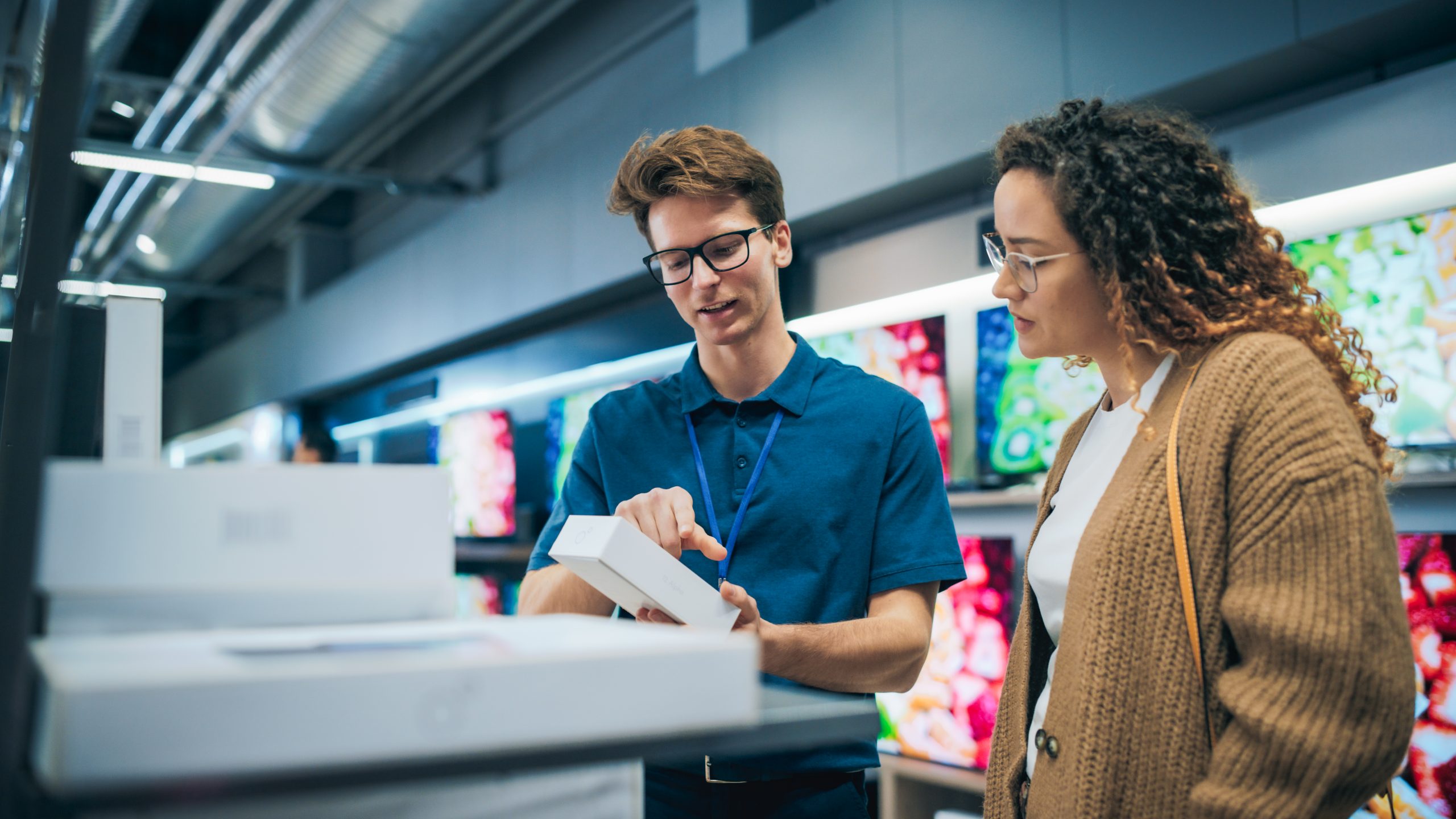 Portrait of a Female Customer Seeking Advice from Retail Home Electronics Expert. Hispanic Girl Explores Smartphone Options. Shopper Evaluating Latest Mobile Phone Innovations in a Department Store