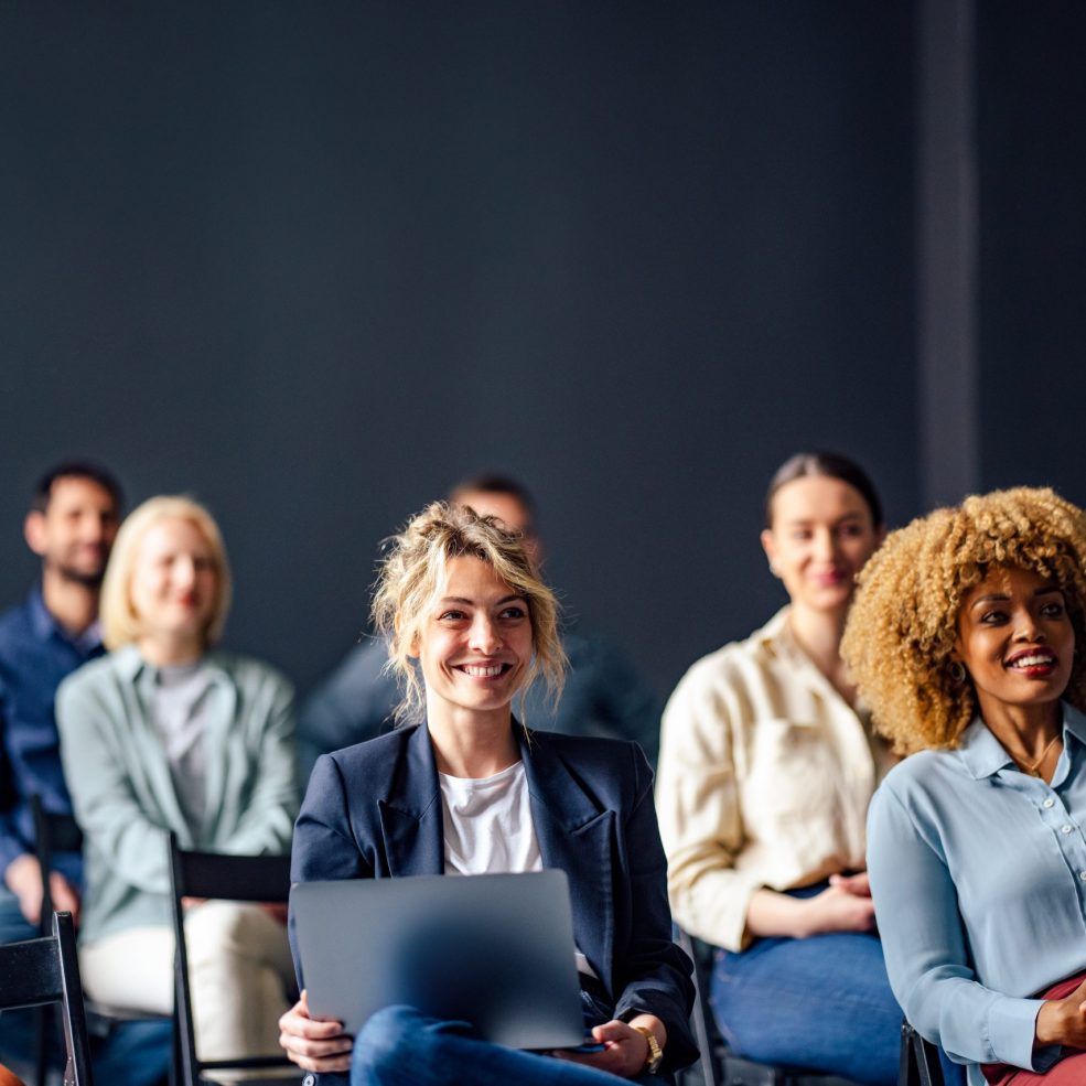 Group of men and women sitting and listening to a seminar. They are smiling.