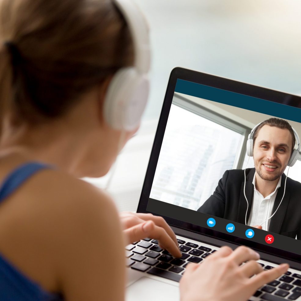 Man and woman in headphones communicating online by video call, looking at full screen videoconferencing app window, webcam videochat, virtual dating, long distance relationships, close up rear view